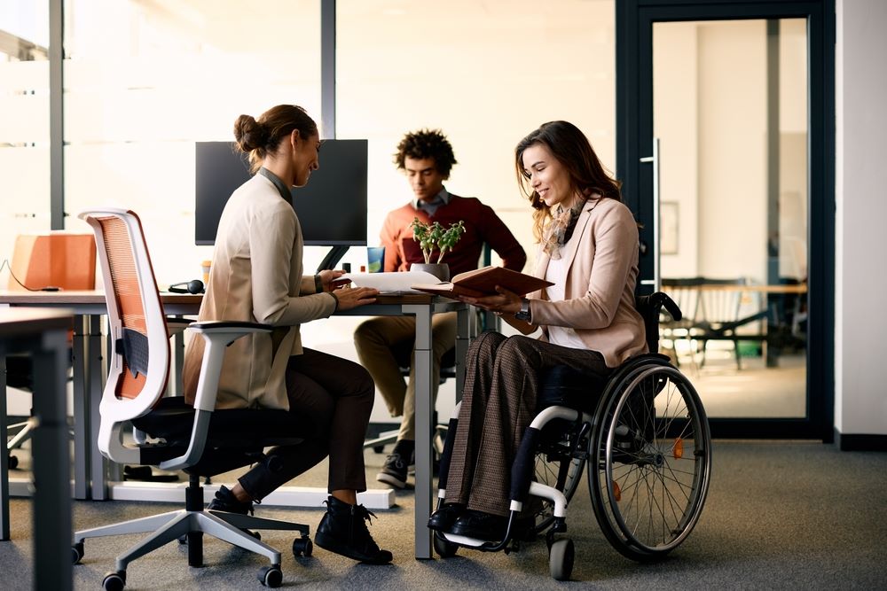 Three colleagues, including a woman in a wheelchair, working together in an office