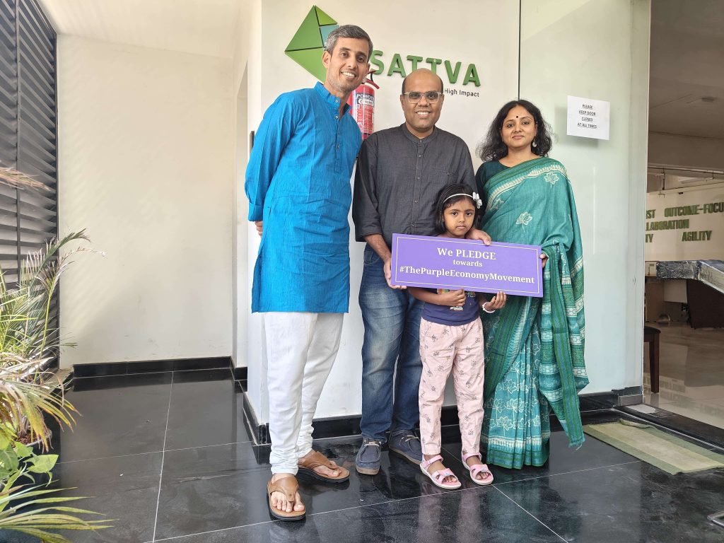 Three adults and a child holding a Purple Economy pledge sign outside an Sattva office.
